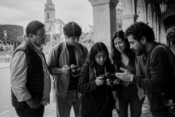 Un guía explicando el manejo de una cámara de 35 mm a un grupo pequeño, bajo los portales de Tequisquiapan